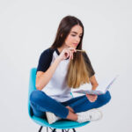 Estudante sentada com pernas cruzadas em uma cadeira, lendo um caderno, demonstrando o processo de preparação para o ENEM.