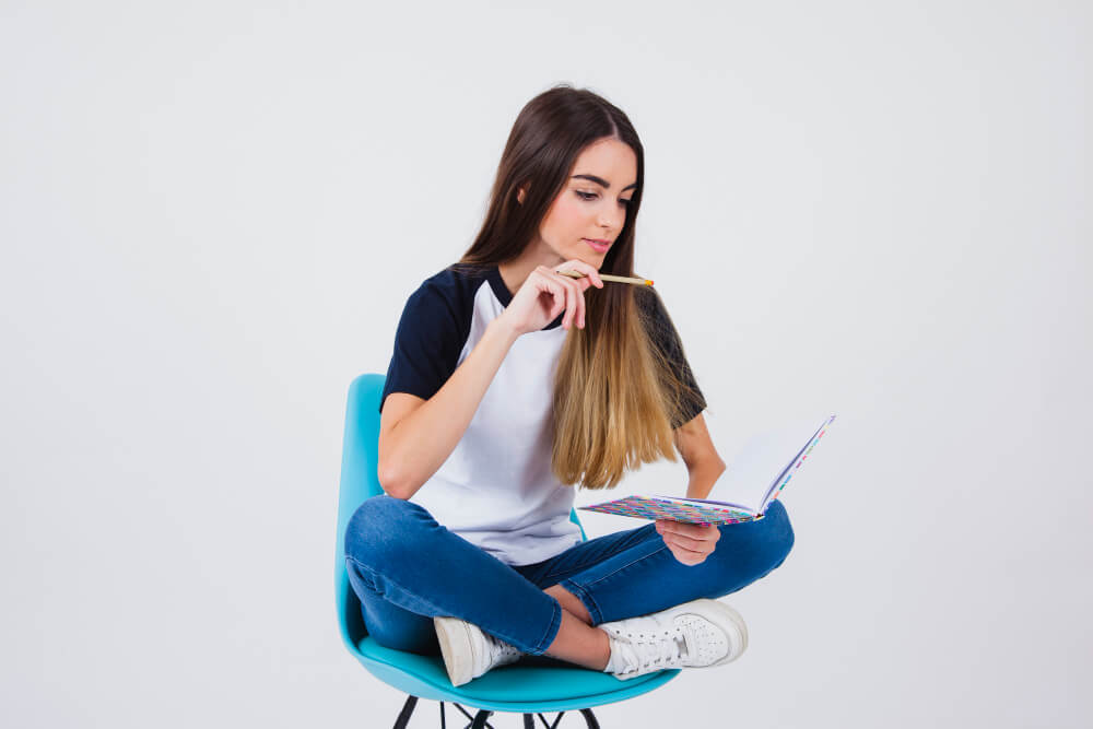 Estudante sentada com pernas cruzadas em uma cadeira, lendo um caderno, demonstrando o processo de preparação para o ENEM.