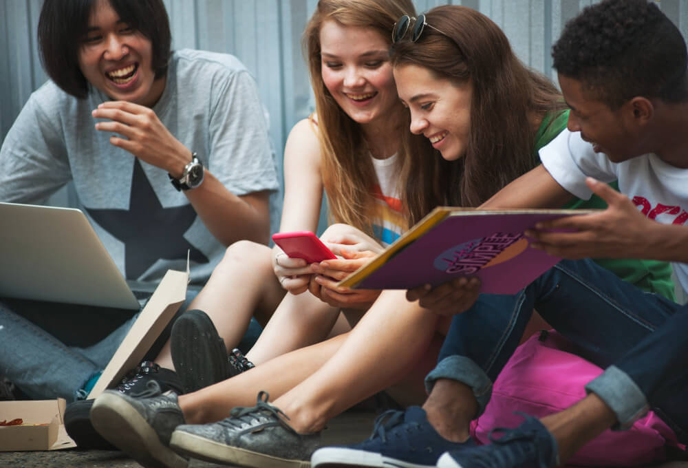 Jovens sentados no chão, rindo, representando a alegria trazida pelo ensino de qualidade.